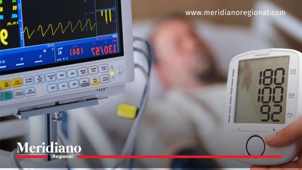 Presión arterial elevada en monitoreo hospitalario - Meridiano Regional Primer plano de tensiómetro digital y monitor cardíaco que indican presión arterial alta (180/105) junto a un paciente hospitalizado desenfocado.