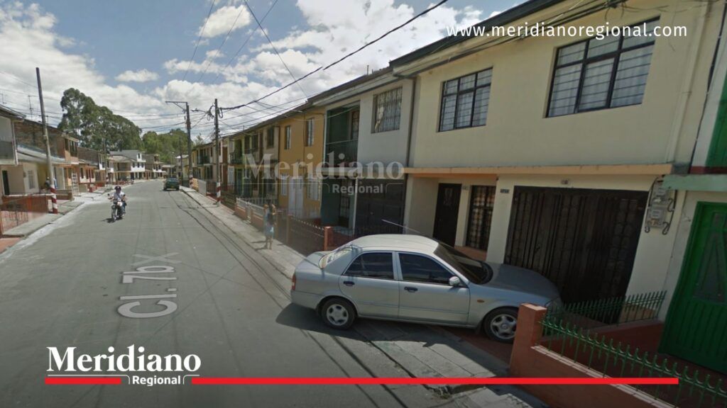 Vista de referencia de una calle residencial del barrio El Libertador en Popayán, con casas de dos pisos, automóvil gris estacionado y motocicleta en circulación, bajo cielo parcialmente nublado