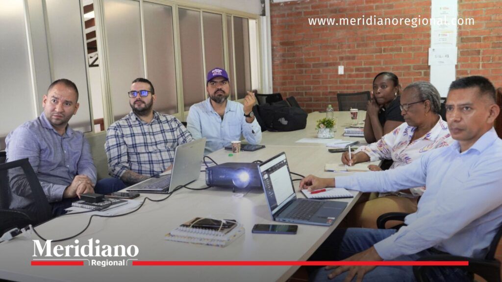 Reunión de trabajo para planificación y toma de decisiones - Meridiano Regional Grupo de personas reunidas en una sala de juntas, trabajando con computadores portátiles y proyectando información en una pantalla.