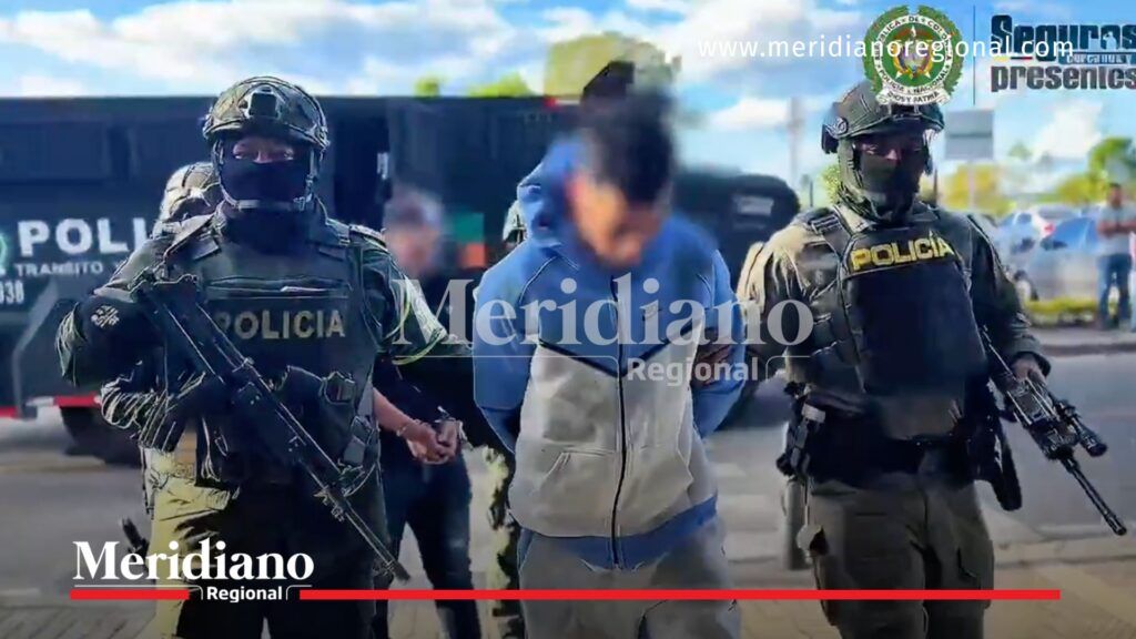 Policías fuertemente armados custodian a un hombre esposado con buzo azul claro, capturado en Popayán por planear un atentado con explosivos.