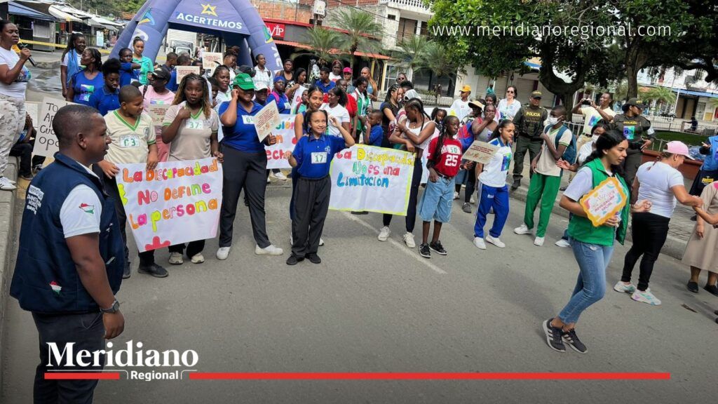 Personas participando en la Maratón de los Sueños en Puerto Tejada con carteles sobre inclusión y discapacidad, acompañados por autoridades locales.