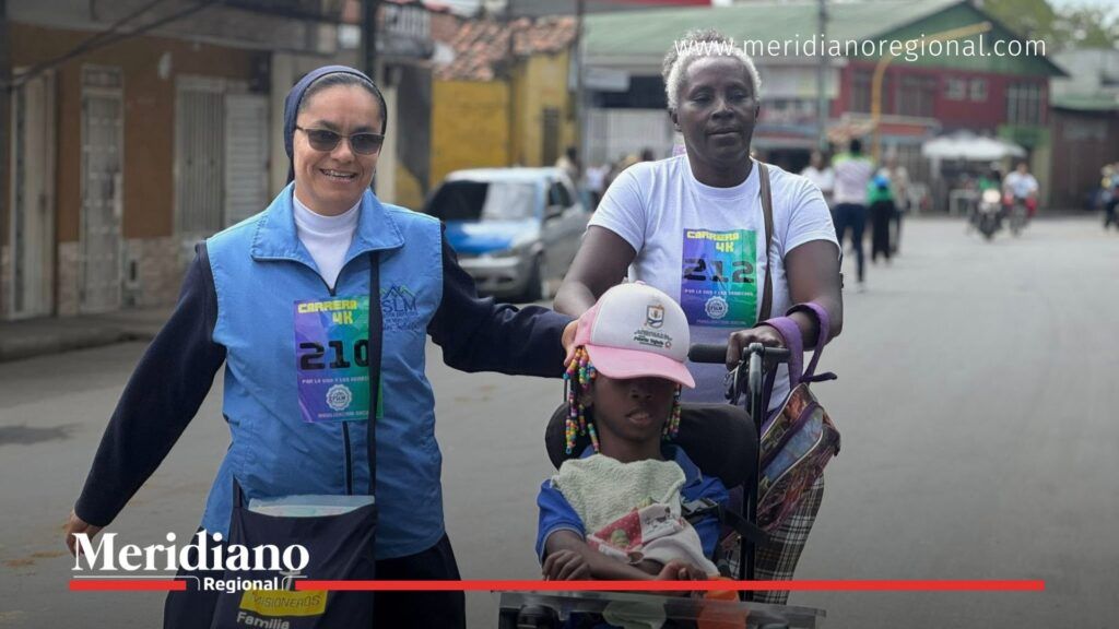 Madre lleva a su hija con discapacidad en silla de ruedas durante la Maratón de los Sueños en Puerto Tejada, acompañadas por voluntarios del evento.