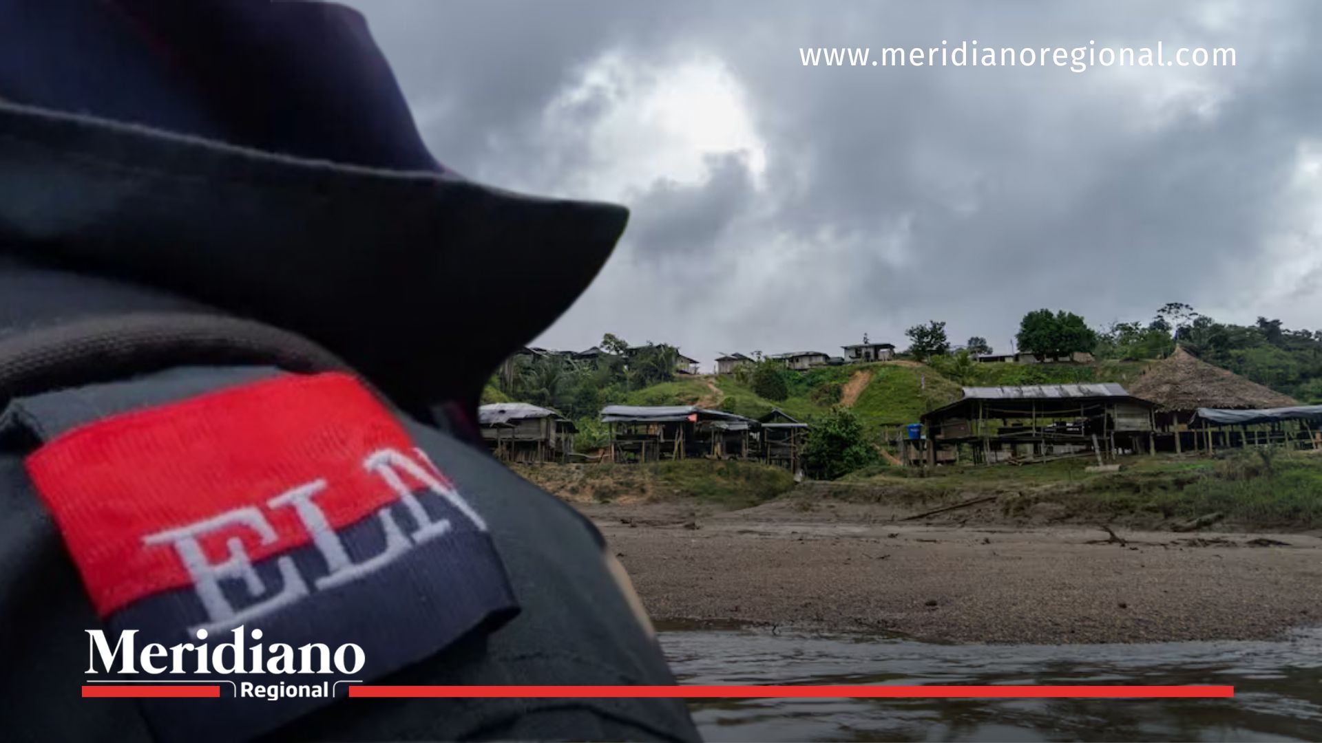Primer plano del uniforme de un integrante de un grupo armado ilegal con emblema visible; al fondo, poblado ribereño del río San Juan en Chocó, zona afectada por la crisis humanitaria en Sipí.