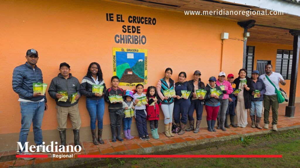 Grupo de estudiantes, docentes y habitantes de Chiribío posando frente a la sede escolar El Crucero, cada uno con semillas entregadas para las huertas escolares durante una jornada ambiental de la Gobernación del Cauca.