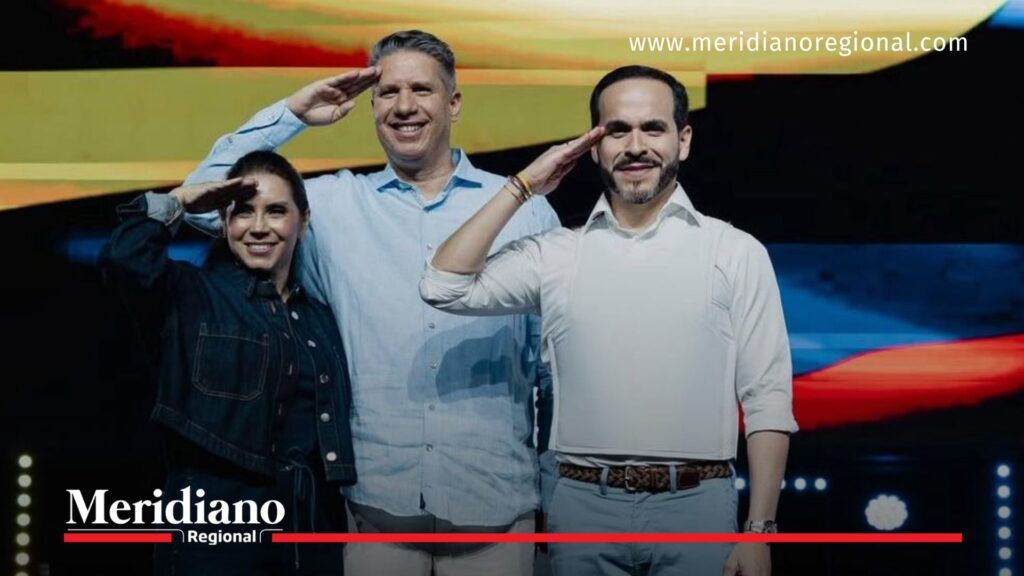 Abelardo de la Espriella saluda en un evento público de campaña, acompañado por dos personas en un escenario iluminado con pantalla de colores.