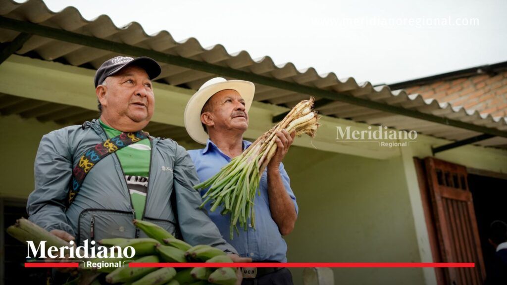 Dos campesinos del municipio de Silvia, Cauca, sostienen productos agrícolas como plátano y cebolla larga durante el evento de entrega de la vía pavimentada entre Usenda, La Estrella y El Jardín.