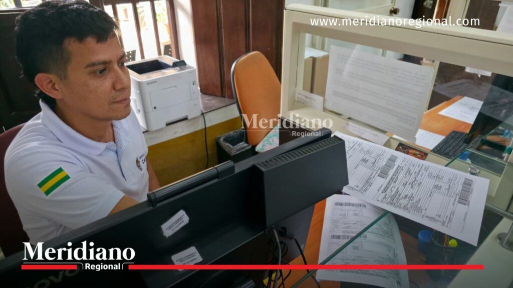 Funcionario de una oficina de rentas del Cauca atiende trámites relacionados con el impuesto vehicular 2026 frente a un computador, junto a formularios de pago y documentos tributarios en un punto de atención al contribuyente.