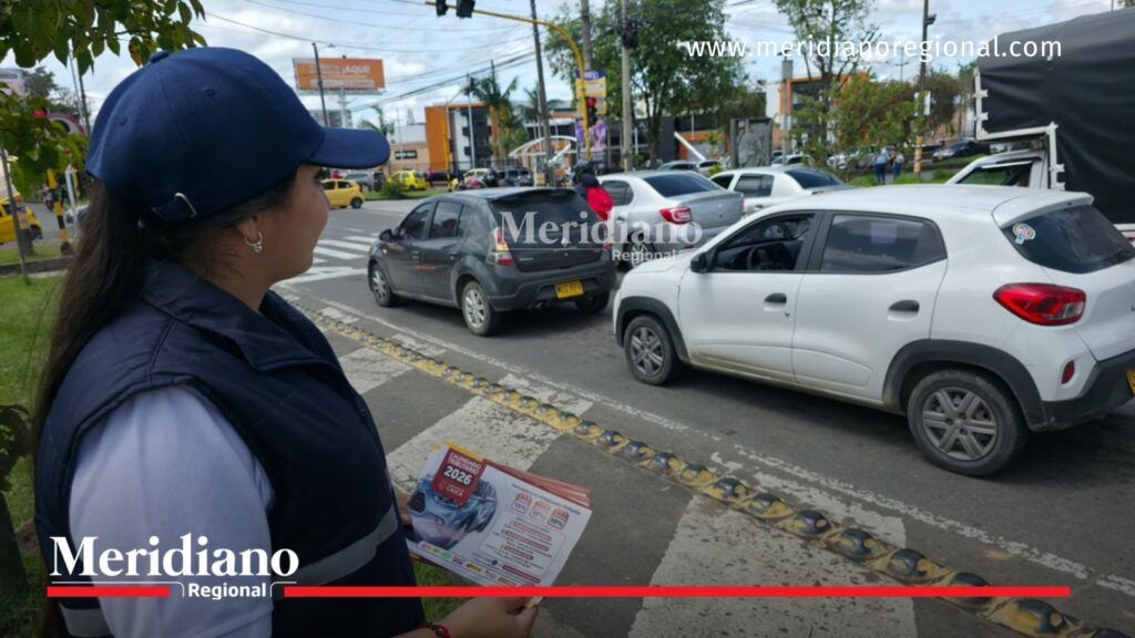Funcionaria de la Gobernación del Cauca entrega información sobre el calendario tributario 2026 a conductores mientras circulan varios vehículos por una vía urbana de Popayán durante una jornada de sensibilización sobre el impuesto vehicular.