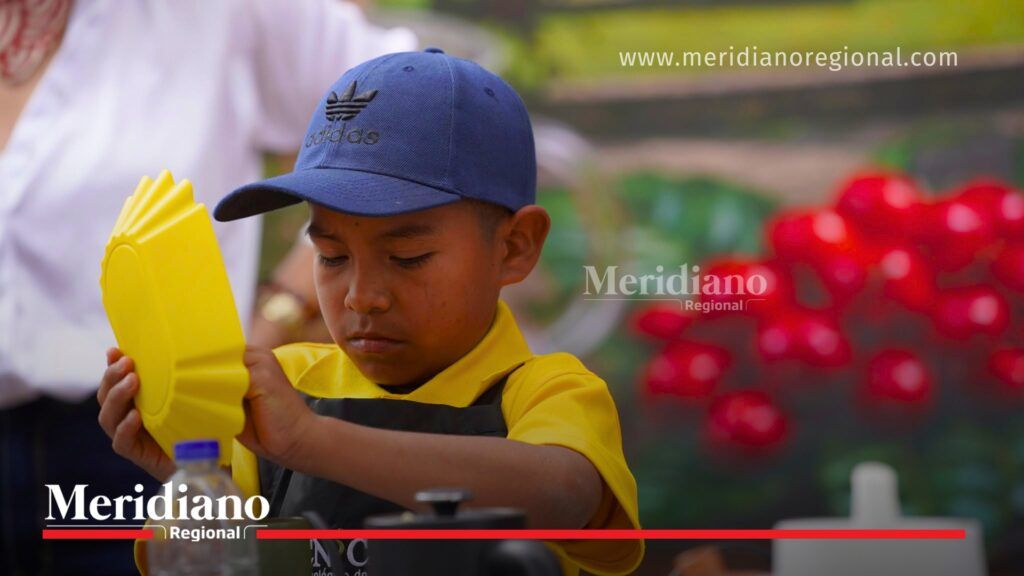 Niño participante del proyecto Escuela y Café realiza una demostración de barismo durante la feria de café en Morales, mostrando sus habilidades en la preparación de cafés especiales.