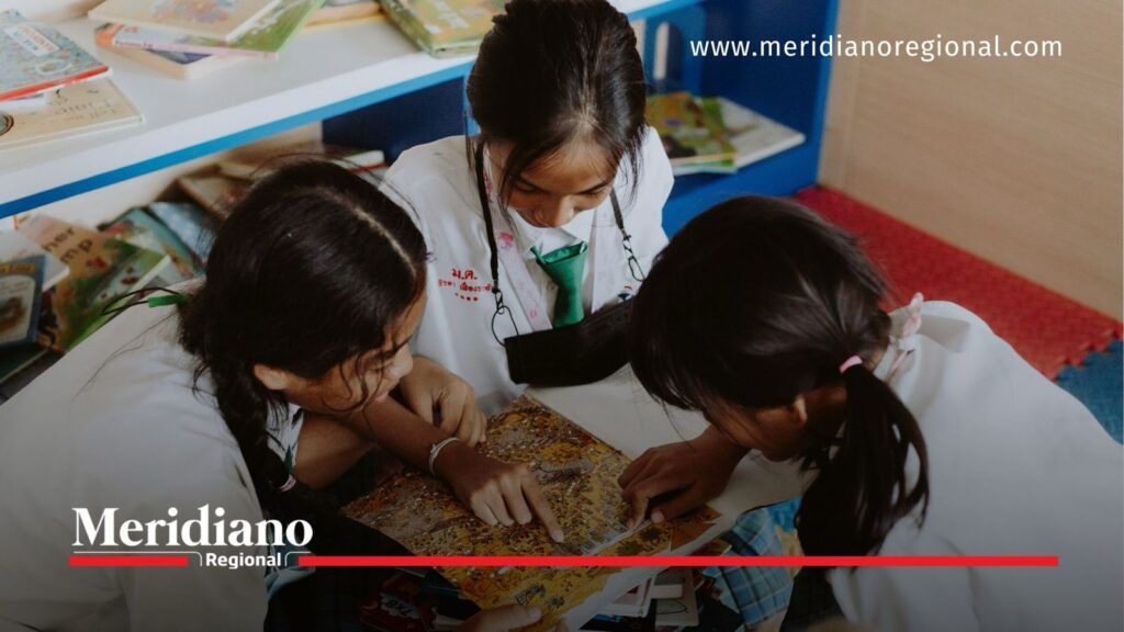 Entornos educativos libres de violencia promueven espacios seguros para el aprendizaje en el Cauca - Meridiano Regional Tres estudiantes realizan una actividad de lectura y aprendizaje colaborativo en una biblioteca escolar, representando la importancia de fortalecer entornos educativos libres de violencia en las instituciones educativas del Cauca.