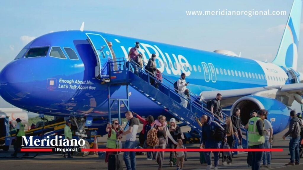 Pasajeros descienden por una escalera de un avión azul de JetBlue estacionado en una pista aeroportuaria.