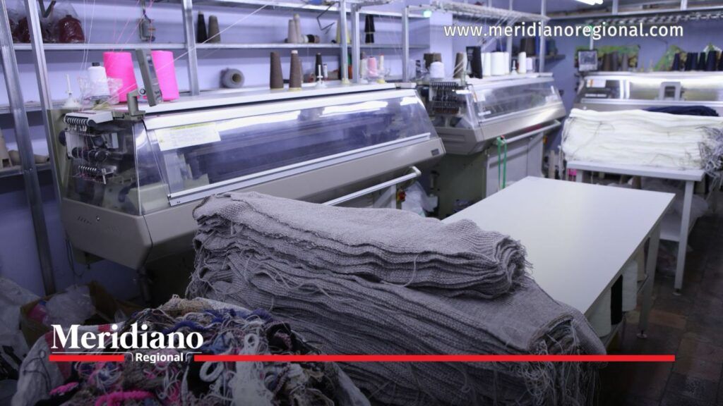 Máquinas industriales de tejido, rollos de hilo y textiles apilados en un taller de confección.