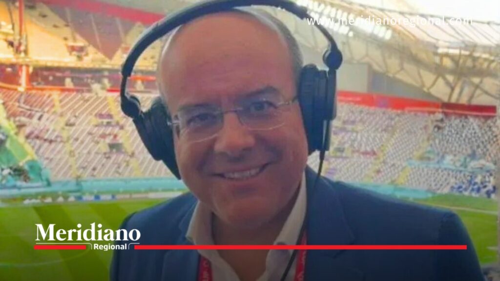 Ricardo Orrego sonríe frente a la cámara con audífonos y gafas durante una cobertura deportiva en un estadio de fútbol.