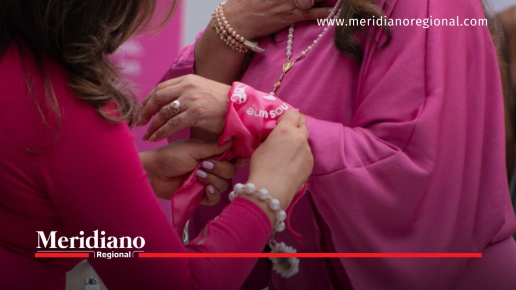 Primer plano de una mujer colocando una cinta rosa en el brazo de otra participante durante una actividad del Mes Rosa.