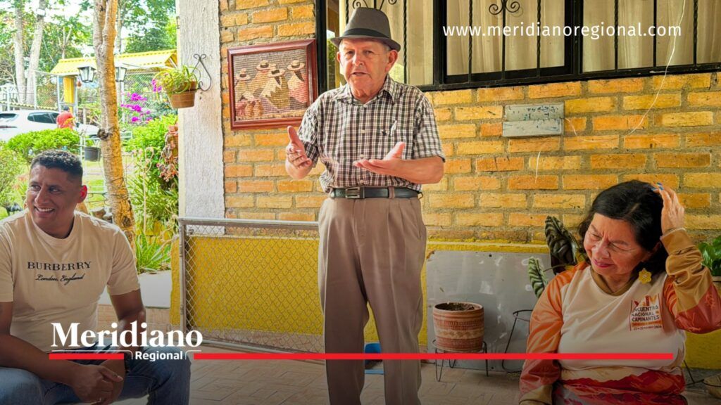 Adulto mayor con sombrero interviene durante un encuentro comunitario ante dos personas sentadas.