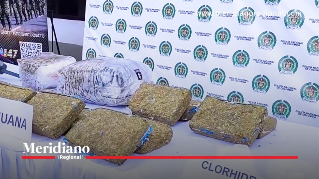 Varios paquetes rectangulares de marihuana, algunos envueltos en plástico, están exhibidos sobre una mesa frente a un fondo con los emblemas de la Policía Nacional de Colombia, durante una presentación oficial en Popayán, Cauca.