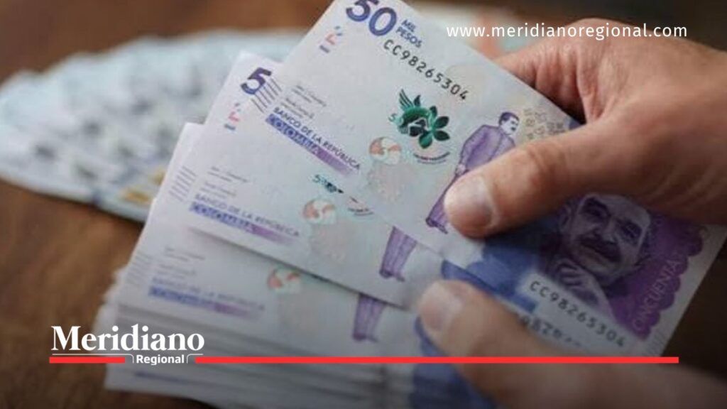 Mano sosteniendo varios billetes colombianos de 50.000 pesos, relacionados con los impuestos y la economía familiar.